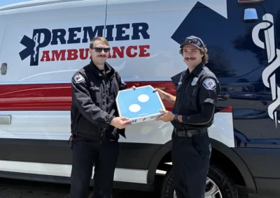 EMS workers hold up a pizza in front of their ambulance