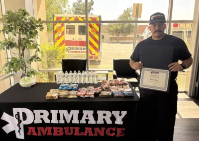 Elias Lopez holds up a certificate of appreciation in front of a Primary Ambulance table holding snacks and drinks