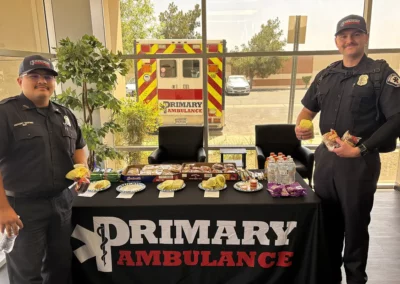 Two EMS workers stand next to a Premier Ambulance table with burritos and snacks