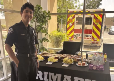 An EMS worker stands next to a Premier Ambulance table with burritos and snacks