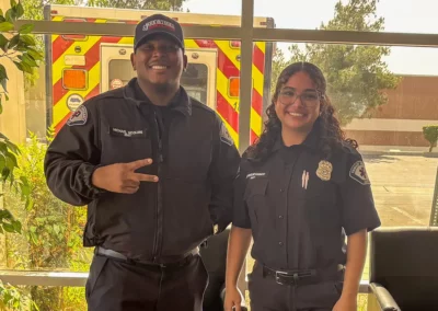 Two EMS workers pose in front of the back of an ambulance