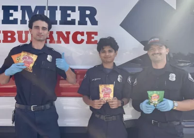 EMS workers stand next to their ambulance, holding up snacks.