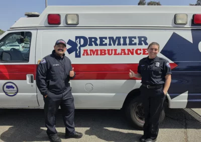 Two EMS workers stand next to their ambulance and give a thumbs up