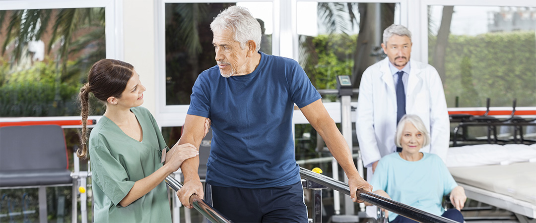 Man using parallel bars with the help of a physical therapist.