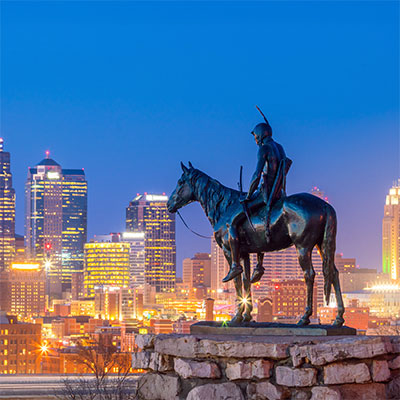 Statue of a man on a horse with the city lights in the background.