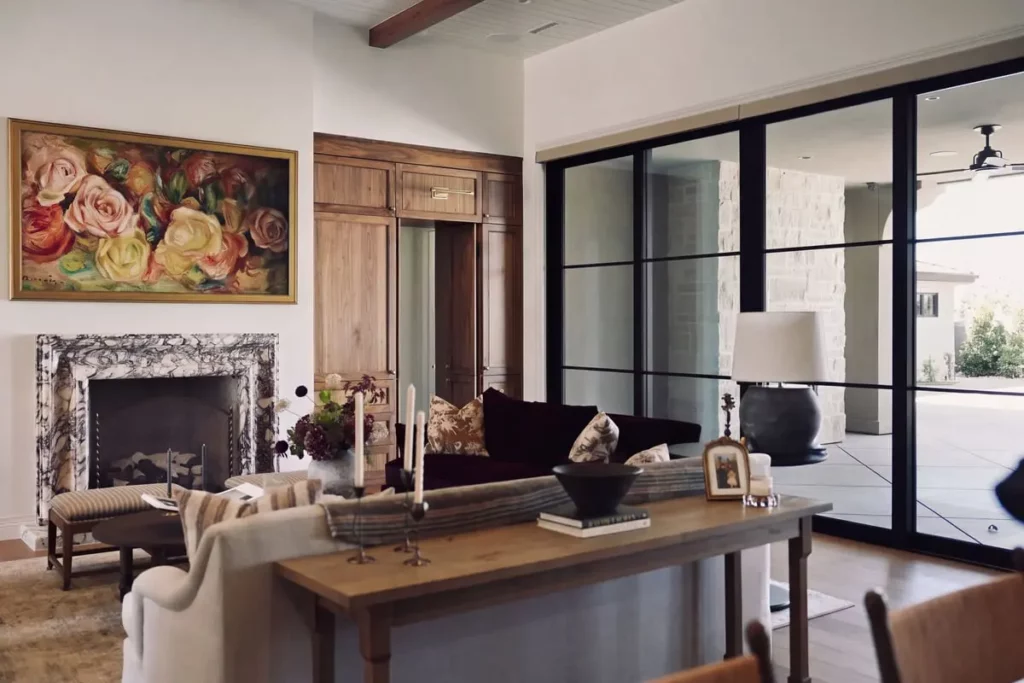 Living room with fireplace, a floral painting on the wall, and large windows