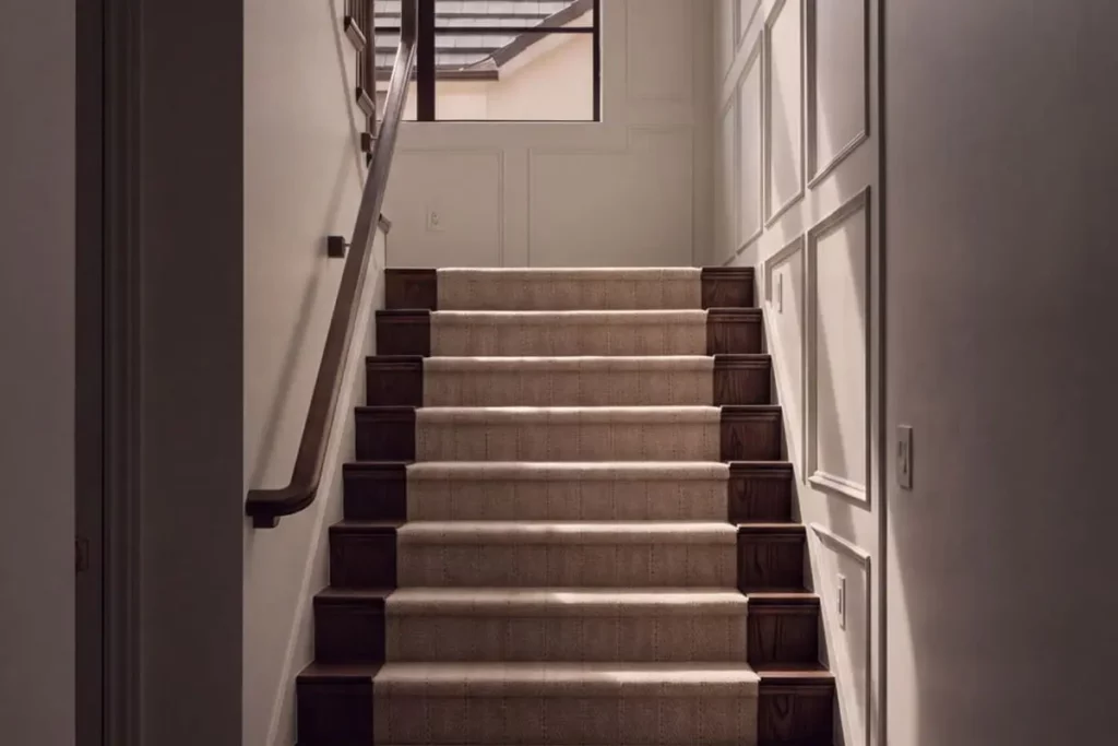 A wooden staircase with a white runner rug