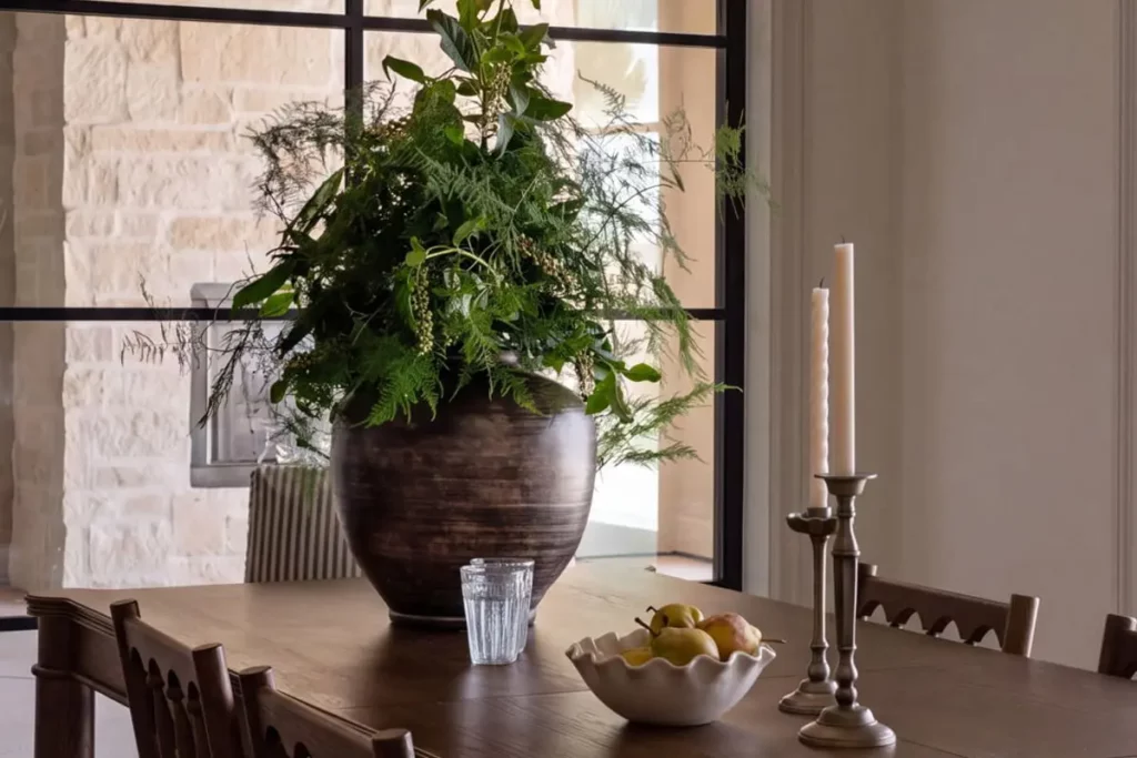 Wooden dining table with greens in a vase, pears in a bowl, and candles